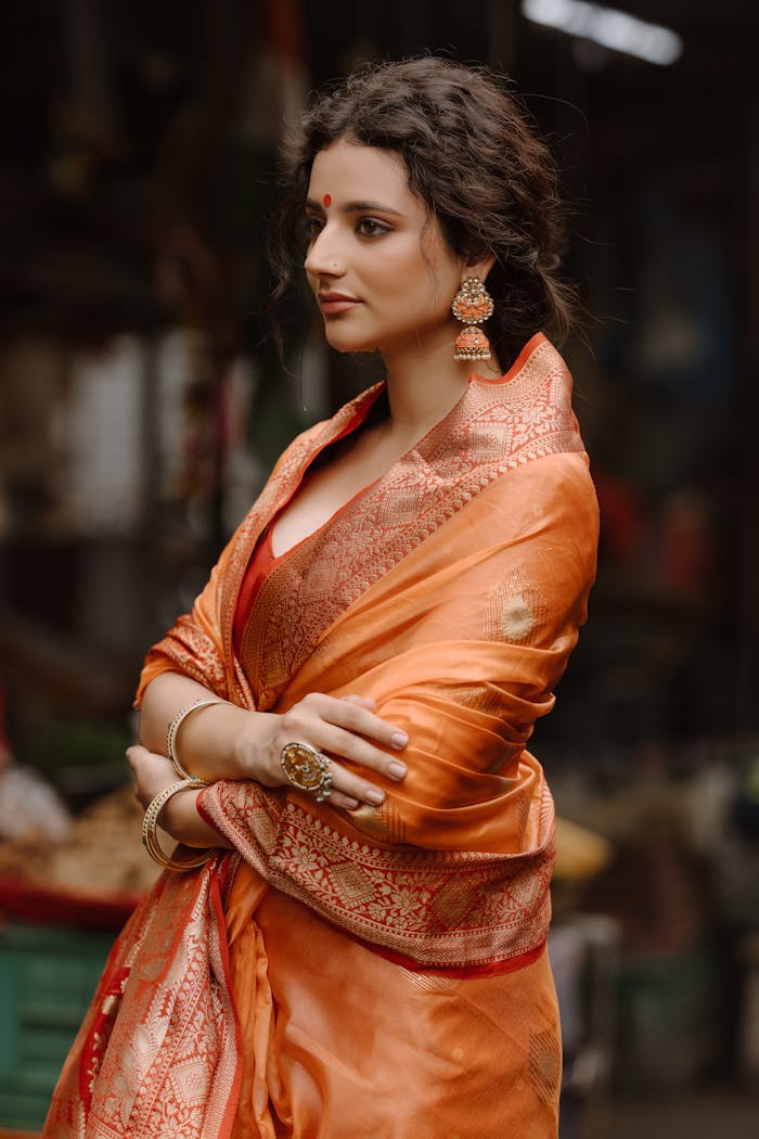 Portrait of an elegant woman wearing a traditional orange saree and jewelry.